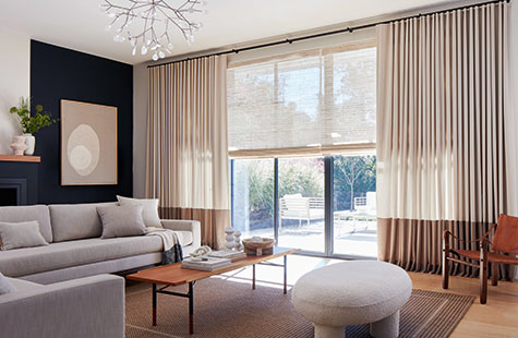 A living room with a blue accent wall had Woven Wood Shades made of Cove in Ash and Ripple Fold Drapery in Andes, Castle Wall