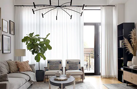 A modern living room with tall windows has Ripple Fold Drapery made of Basket Sheer in Winter which contrasts the black decor