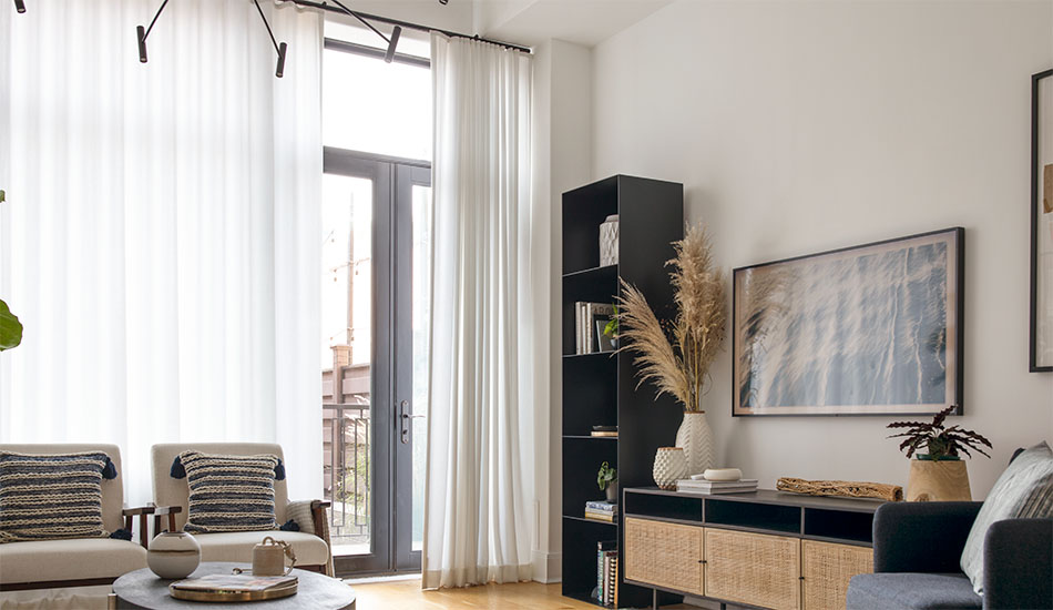 A living room has tall glass doors with minimalist window treatments including Ripple Fold Drapery in Basket Sheer, Winter