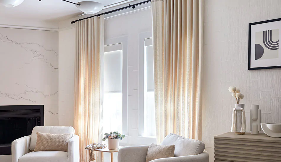 Modern window treatments in a bright family room include ripple fold drapery in a cream color over sleek roller shades