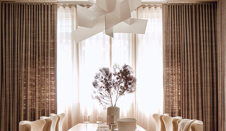 A modern dining room has layered curtains made of Ripple Fold Drapery in Luxe Sheer Linen in Natural and Raw Silk in Graphite