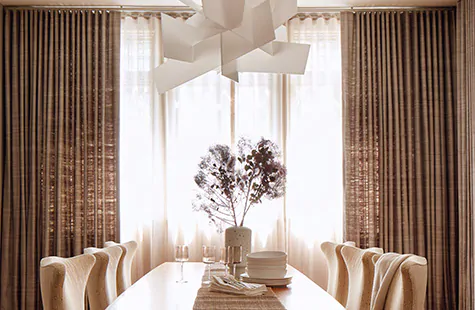 A dining room has layered window treatments of Ripple Fold Drapery in Luxe Sheer Linen in Natural and Raw Silk in Graphite