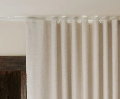 A close-up shot of alabaster-colored thermal curtains, specifically ripple fold drapery, hanging along a track