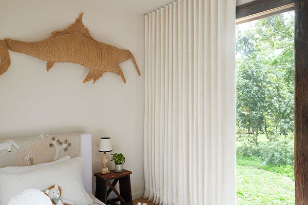 A bedroom with warm creamy tones features Ripple Fold Drapery made of Claude Stripe in Alabaster for texture and privacy