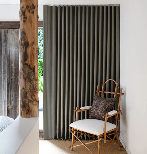 A rustic bedroom has grey curtains in the Ripple Fold Drapery style made of material from Nate Berkus' collection