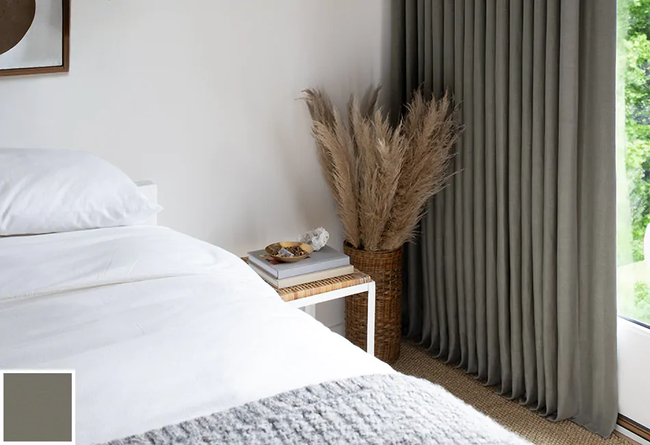 A guest bedroom features a grass feather arrangement beside a small coffee table and ripple fold drapes