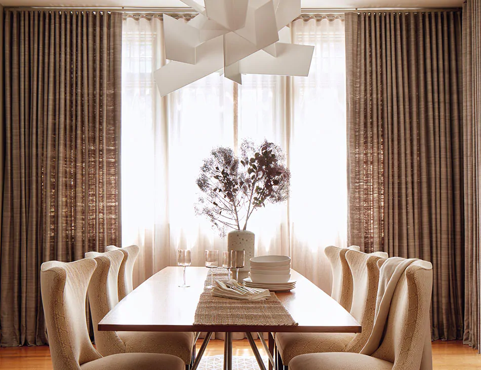 A modern dining room has Raw Silk curtains in Graphite layered with Luxe Sheer Linen curtains in natural for contrast