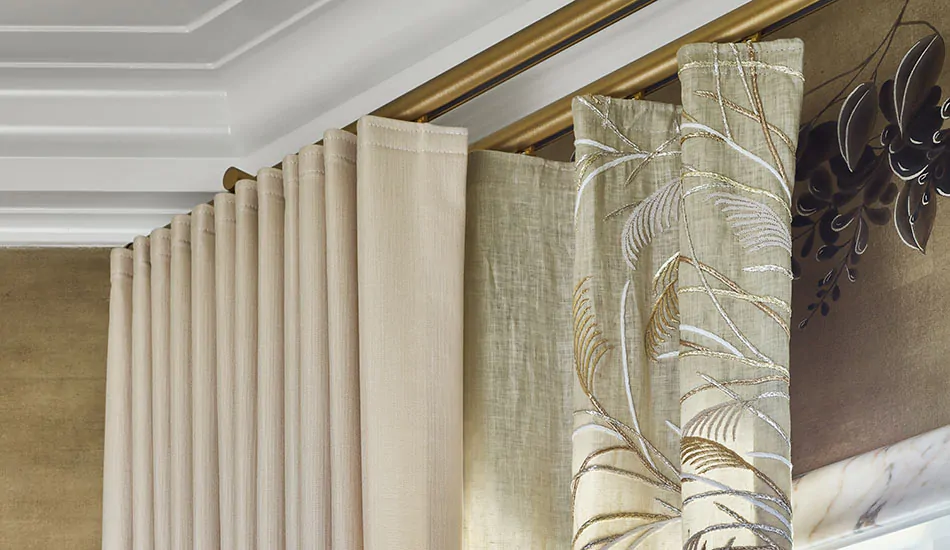 A gold double curtain rod has layered curtains of Ripple Fold Drapery in Sheer Muslin Embroidered Fabric and Neblina in Sand