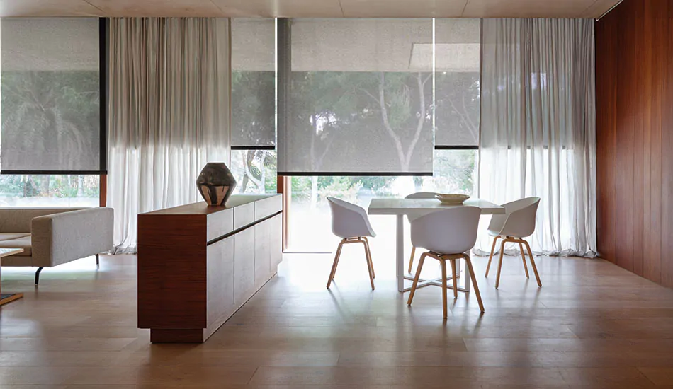 A modern table sits in front of huge windows with curtain sheers of Sheer Wool Blend in Grey Owl layered with Solar Shades