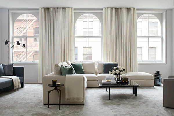 A bright living room features curtains for arched windows made of Ripple Fold Drapery in Wool Flannel, Glacier