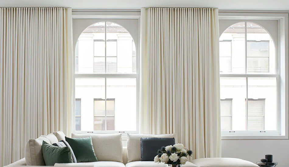 A large bright living room features arched windows framed by Ripple Fold Drapery made of Wool Flannel in Glacier