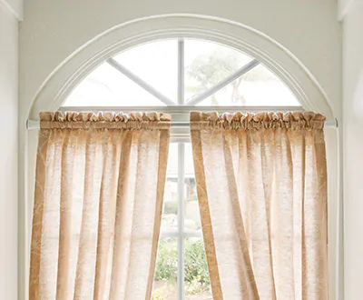 A small full chord arch window has curtains for arched windows made of Chinoiserie in Blush installed below the arch