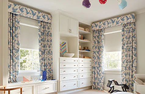 A kids room has layered window treatments of Ripple Fold Drapery of Family of Cranes and Roller Shades of Ava in Birchwood