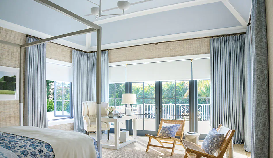 A large bedroom with blue, white nad beige colors features corner window curtains made of Vanda in Sky