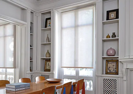 A Roller Shade made of Chelsea in Sand allows light to filter into a mid-century modern dining room with colorful chairs