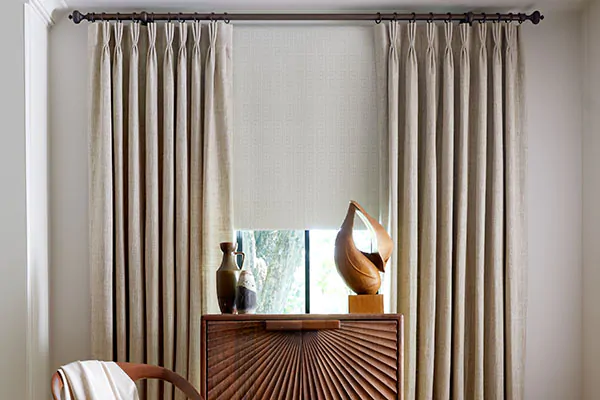 Transitional window treatments of a Roller shade in Corfu and Pinch Pleat Drapery in Shoreline complement intricate furniture
