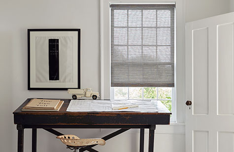 Bamboo roller blinds made of Roller Shades in Jackson, Sand, cover a small window in an office with a dark wood table