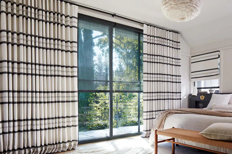 To compare light filtering vs blackout a bedroom has black Solar Shades and bold striped drapery with blackout lining