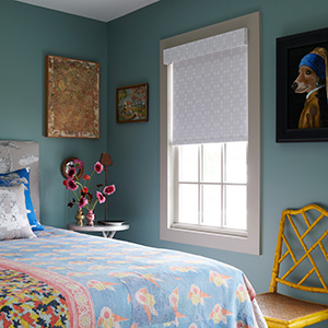 A bright teal bedroom has a blackout Roller Shade that shows the superior light blocking of shades between blinds vs shades