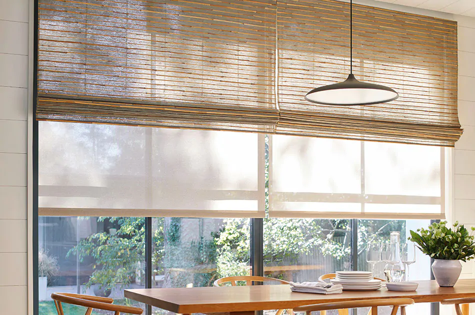 Bamboo blinds made of Reed in Slate are layered with Roller Shades made of Sullivan in Sand over tall dining room windows