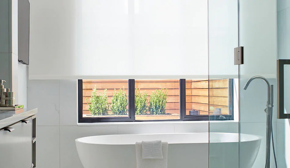Roller Shades made of Techno in White offer bathroom window privacy for a modern white bathroom with a standalone tub