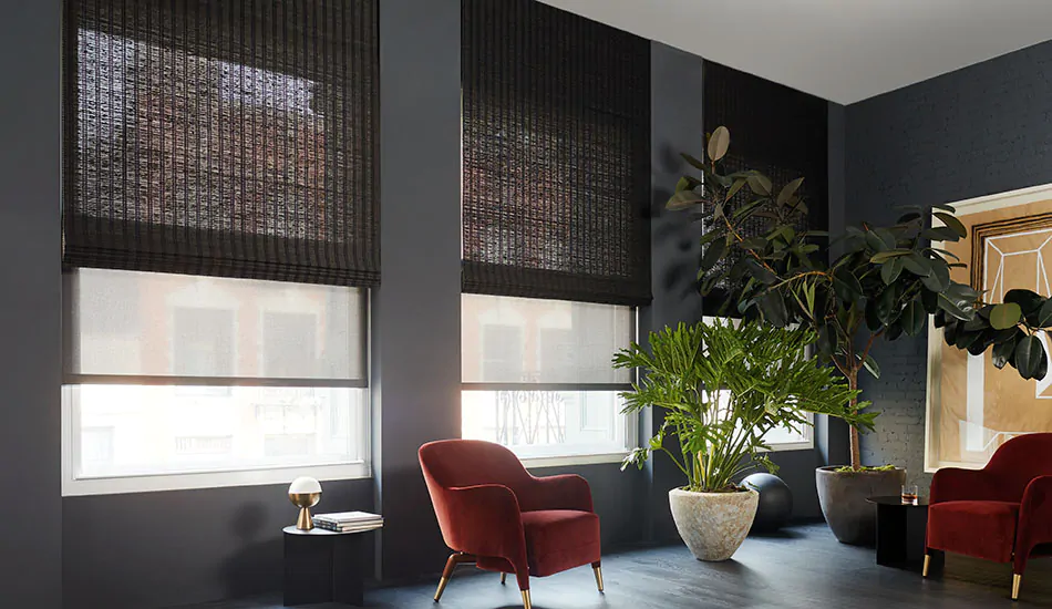 Contemporary window treatments in a dark mid century modern room include dark gray solar shades under black woven wood shades
