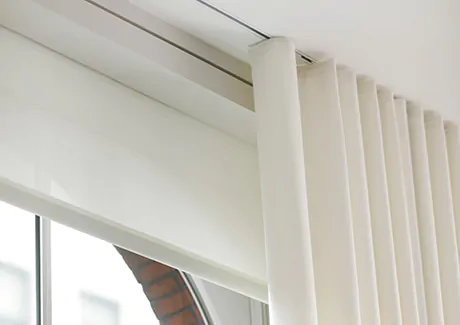 Ripple Fold Drapery in an off-white color hangs from a ceiling-mounted track system which affects how to measure for curtains