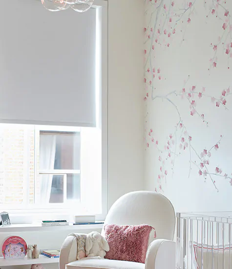 An off-white nursery with pink accents has blackout shades for nursery windows made of Roller Shades in Cora Blackout, White