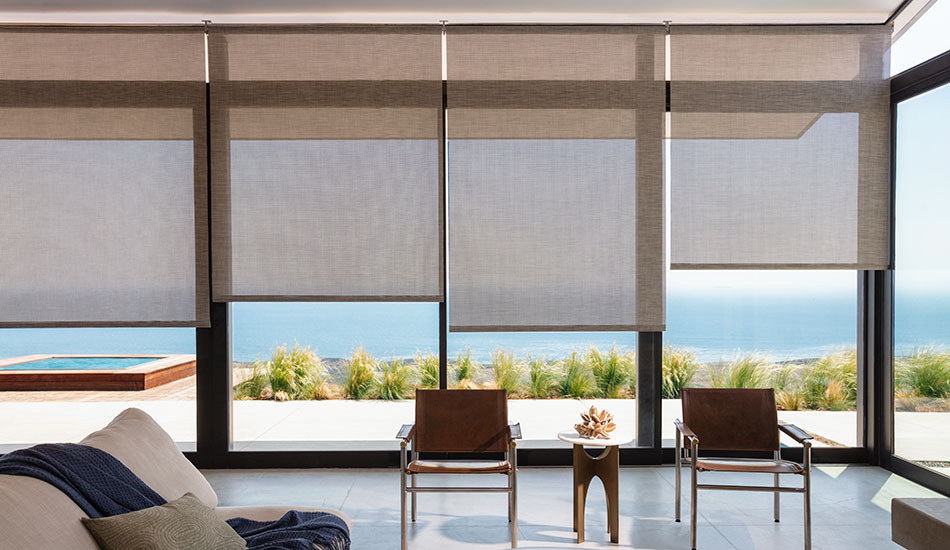 Roller Shades made of Naomi in Honey are used as sunroom window treatments with tall windows looking out on a beach