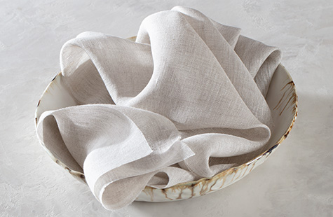 Fabric made of Luxe Sheer Linen sits invitingly in a distressed ceramic bowl on a white marble table