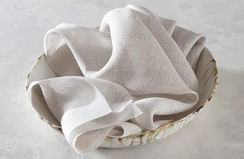 A pile of Roman Shade swatches made of Luxe Linen piled decoratively in a rustic bowl on a white marble table