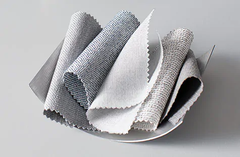 Roman Shades swatches made of Sunbrella Designer materials in cool neutral tones are piled in a metal bowl 