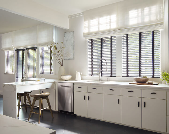 A white kitchen with Flat Roman Shades and Wood Blinds.