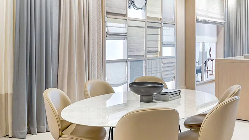 A round white table with cream chairs sits in a custom window treatment showroom with drapery, shades and blinds displayed.