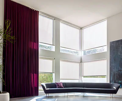 A modern living room features corner window curtains made of Wool Sateen in Aubergine and Solar Shades made of 1% in Grey