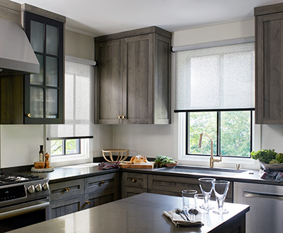 A modern kitchen with grey cabinets has Solar Shades that let light through showing the difference between blinds vs shades