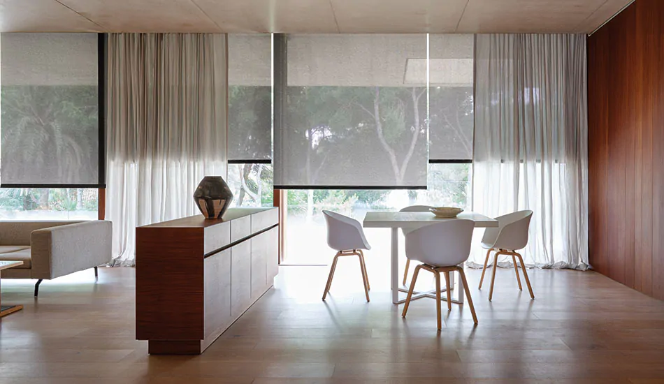 A dining area with an open concept features tall, wide windows with Solar Shades and Ripple Fold Drapery in light grey tones
