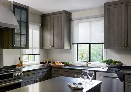 A kitchen with warm grey cabinets and ivory walls has Solar Shades made of Sunbrella 3% Solistico in Ash for softened light