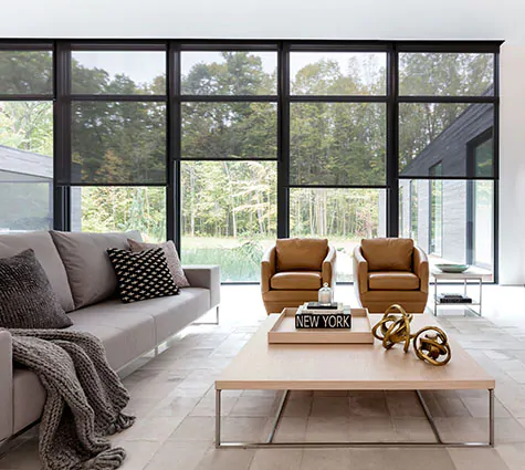 A modern, minimalist living room has tall windows with Solar Shades made of 10% material in Black for a view outside
