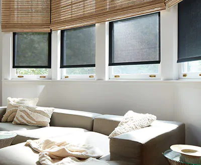 Window treatments for bay windows include Solar Shades, layered under Woven Wood Shades in a family room