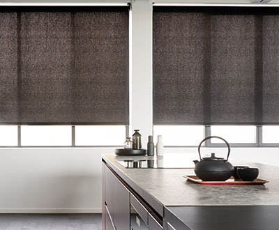 Two solar shades for windows with an onyx color filtering light in a modern kitchen full of dark wooden accents
