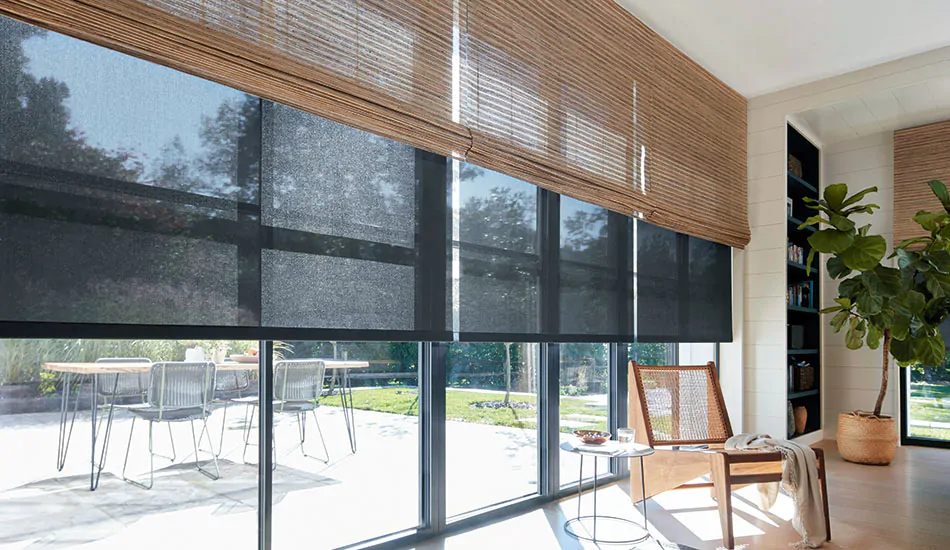 A large room with tall, wide windows has Woven Wood Shades made of Cove in Beige over Solar Shades made of 5% in Black