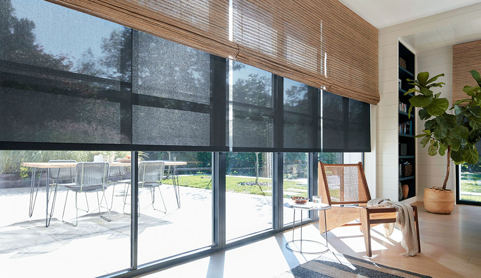 A sunny sitting room with black solar shades under woven wood shades helps answer the question what is a solar shade