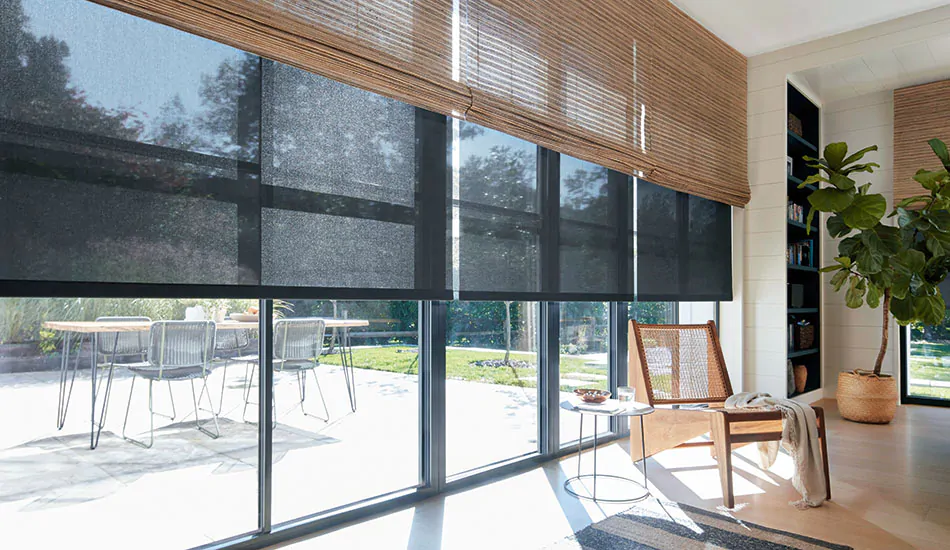 A sunny sitting room with black solar shades under woven wood shades helps answer the question what is a solar shade