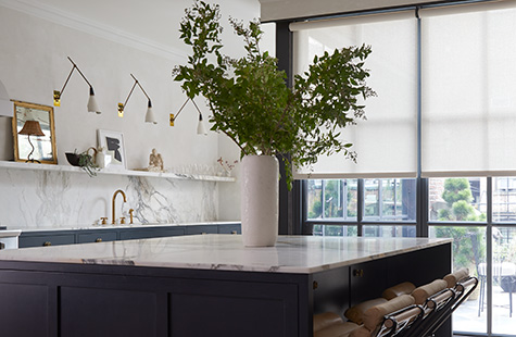 A bright kitchen has a large island and tall windows with Solar Shades and Ripple Fold Drapery in creamy colors