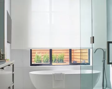 Light Filtering Solar Shades featured over a large window in all white bathroom with a white freestanding bathtub