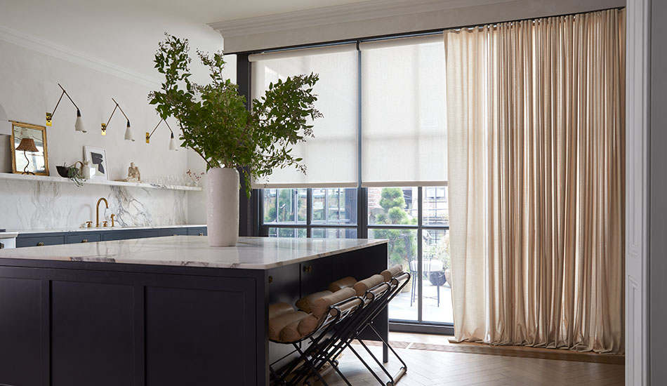 Modern window treatments in a kitchen include warm-toned, modern drapery over floor-to-ceiling windows with beige solar shades
