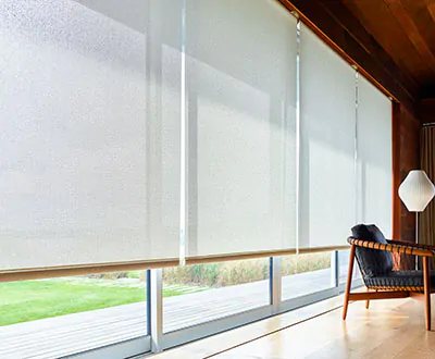 A row of floor-to-ceiling windows are covered by a row of solar shades that allow light into the large bedroom