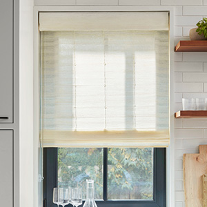 In a simple farmhouse kitchen, a Standard Woven Wood Shade made of Coastline in Muslin covers a window above the counter