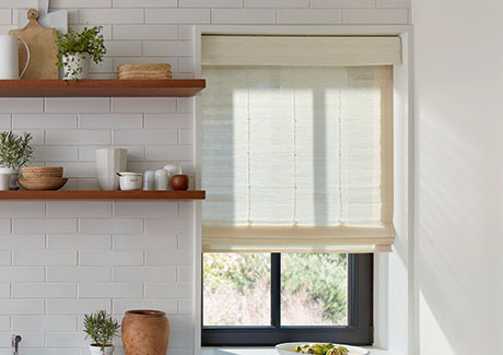A Standard Woven Wood Shade made of Artisan Weaves Coastline in Muslin is inside mounted in a farmhouse kitchen window